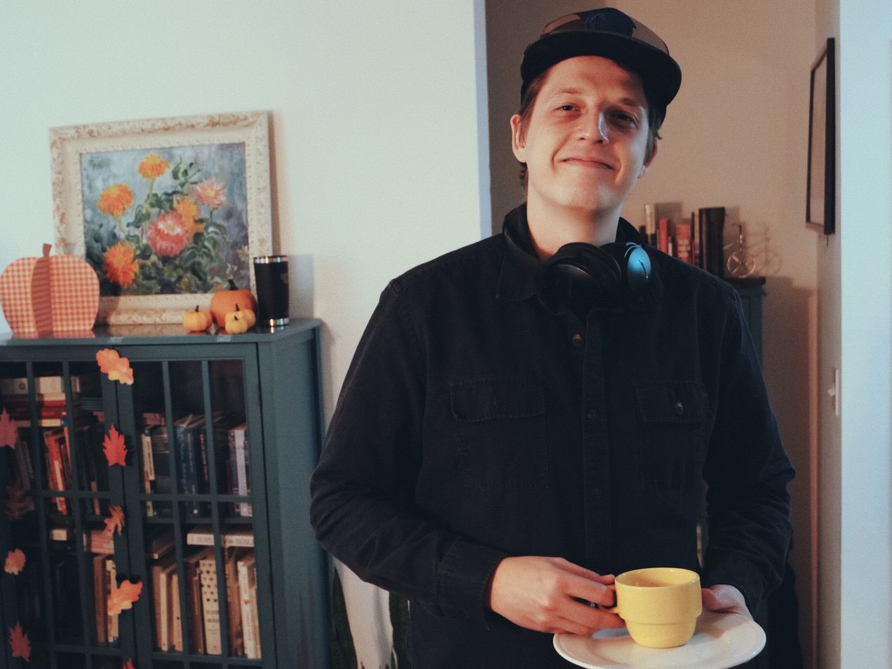 Young man in front of a bookcase at the Covenant Church meeting holding a yellow cup of tea and saucer