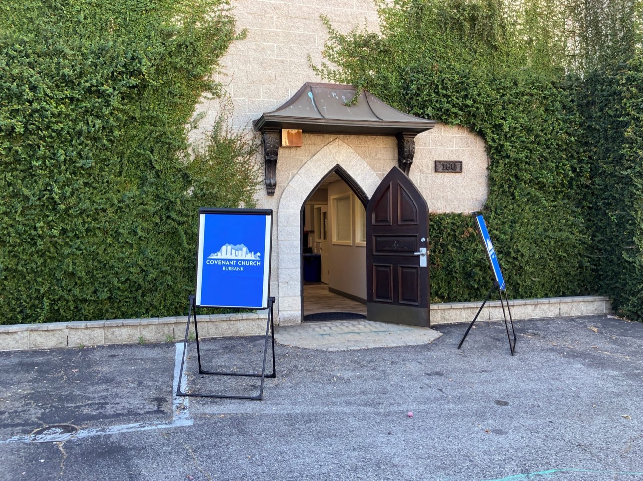 The arched wooden door at the entrance of Covenant Church in Burbank, with the church's blue A-frame sign welcoming visitors in.